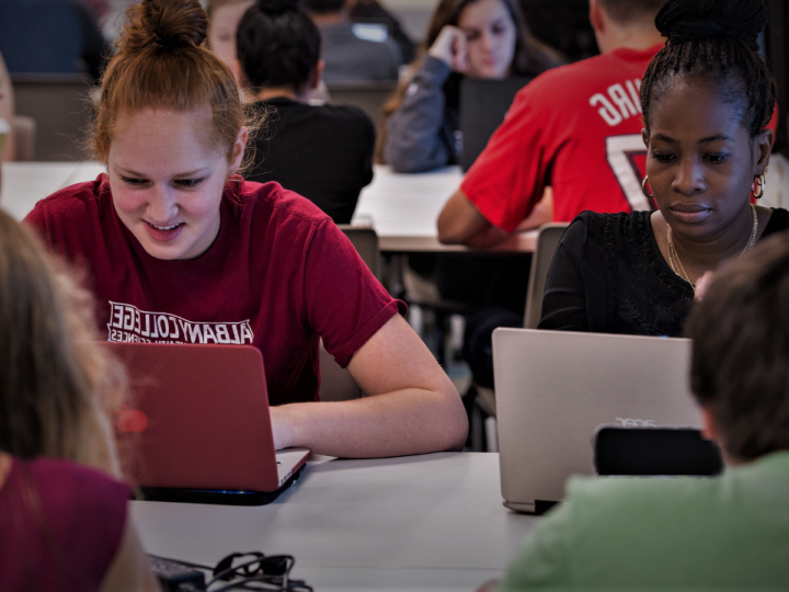 A student and faculty member sit together on laptops